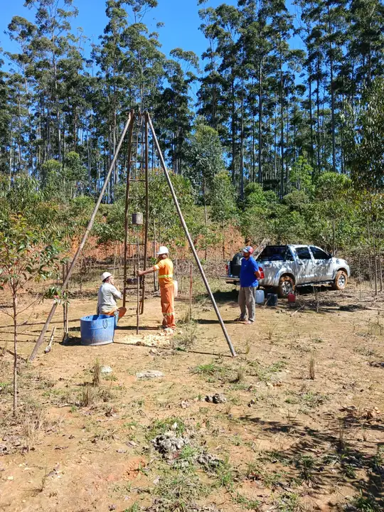 Tripé de sondagem SPT montado em terreno de obra, com a equipe de campo e o reservatório de água da lavagem